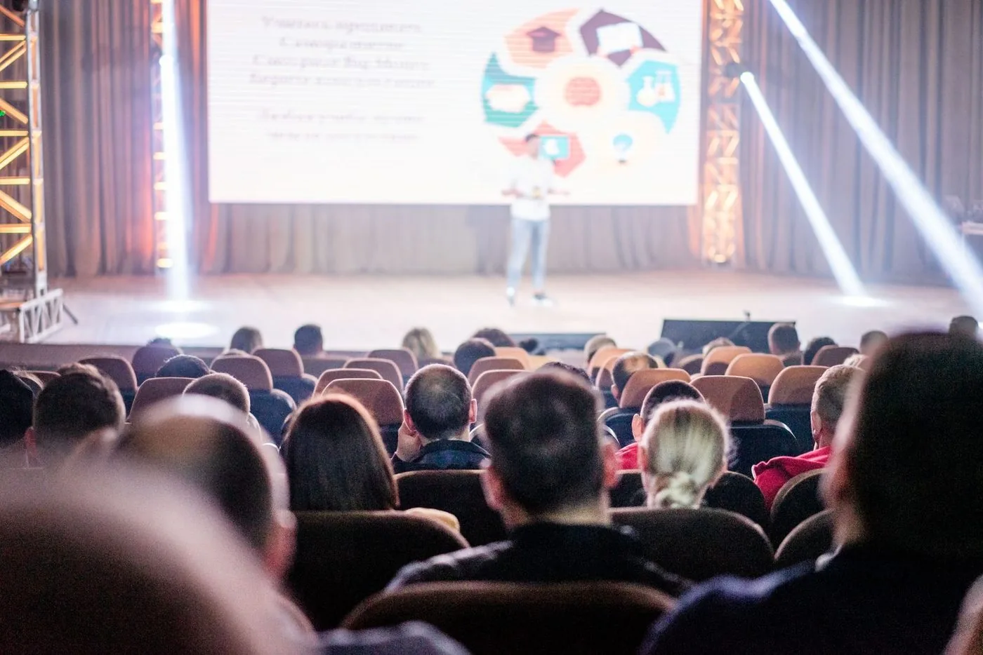 Plateia de costas em auditório, com o palco ao fundo