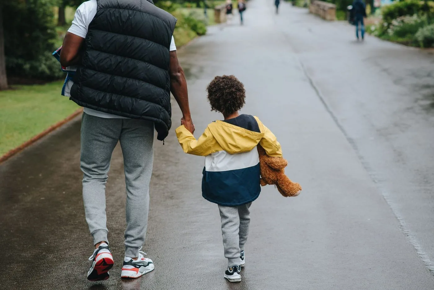 Adulto e criança de mãos dadas, de costas, caminhando no parque